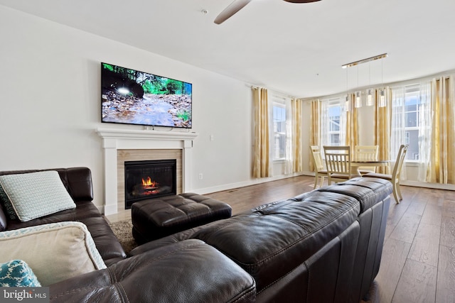 living area with a tiled fireplace, ceiling fan, wood-type flooring, and baseboards