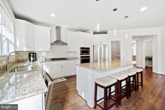 kitchen featuring a sink, appliances with stainless steel finishes, wall chimney range hood, and decorative backsplash