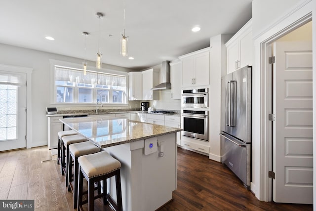 kitchen featuring stainless steel appliances, tasteful backsplash, dark wood-type flooring, a kitchen island, and wall chimney exhaust hood