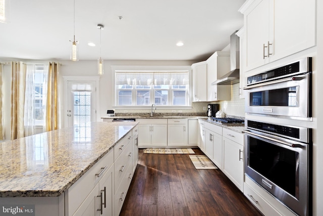 kitchen featuring dark wood finished floors, tasteful backsplash, appliances with stainless steel finishes, white cabinetry, and wall chimney range hood