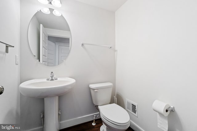 half bath featuring toilet, baseboards, visible vents, and wood finished floors