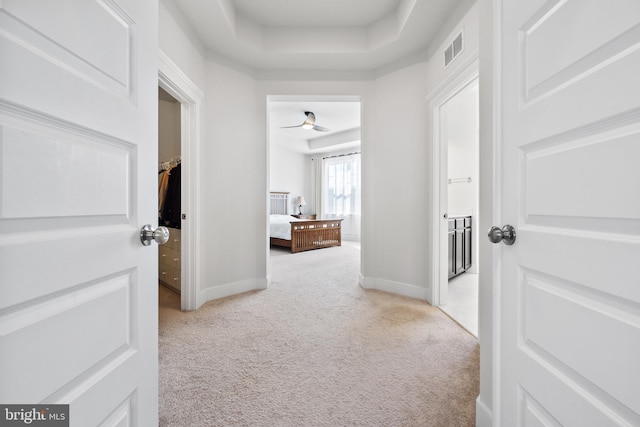 hall featuring a raised ceiling, light colored carpet, visible vents, and baseboards