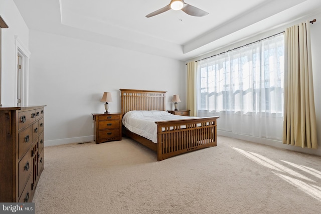 bedroom featuring light carpet, ceiling fan, a tray ceiling, and baseboards