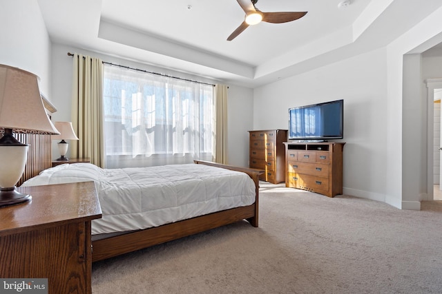 carpeted bedroom with a ceiling fan, a tray ceiling, and baseboards