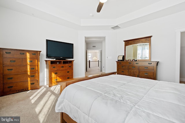 bedroom featuring light carpet, visible vents, a raised ceiling, and a ceiling fan