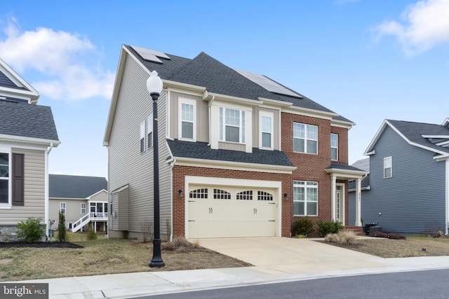 view of front of house featuring a garage, solar panels, brick siding, concrete driveway, and roof with shingles