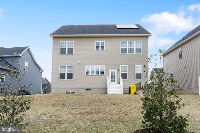 rear view of house featuring entry steps, a lawn, and solar panels