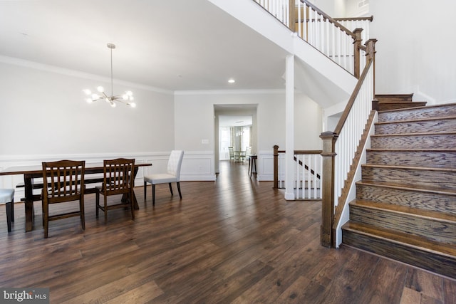 dining space featuring a chandelier, a decorative wall, a wainscoted wall, dark wood finished floors, and crown molding