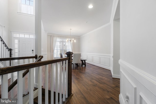 corridor featuring a wainscoted wall, ornamental molding, dark wood-type flooring, a decorative wall, and a notable chandelier