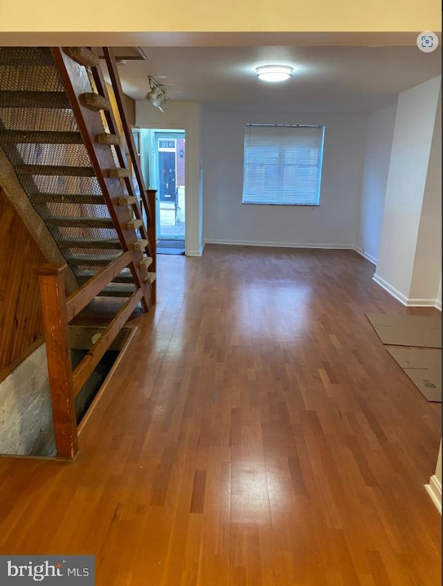 unfurnished living room featuring baseboards, stairway, and wood finished floors