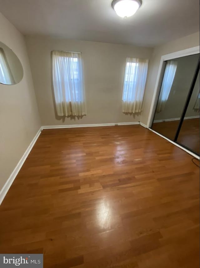 unfurnished bedroom featuring a closet, multiple windows, baseboards, and wood finished floors