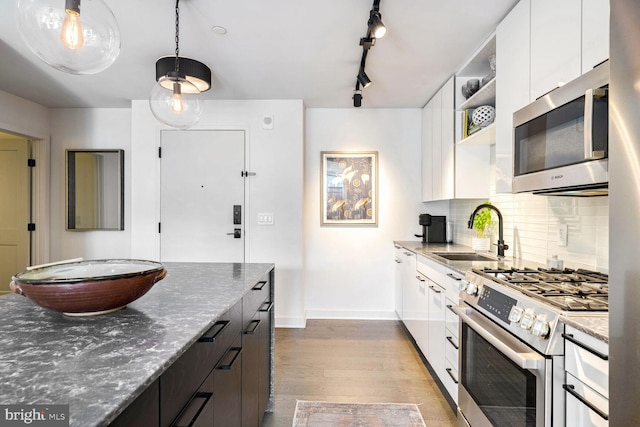 kitchen with a sink, stainless steel appliances, white cabinetry, open shelves, and backsplash