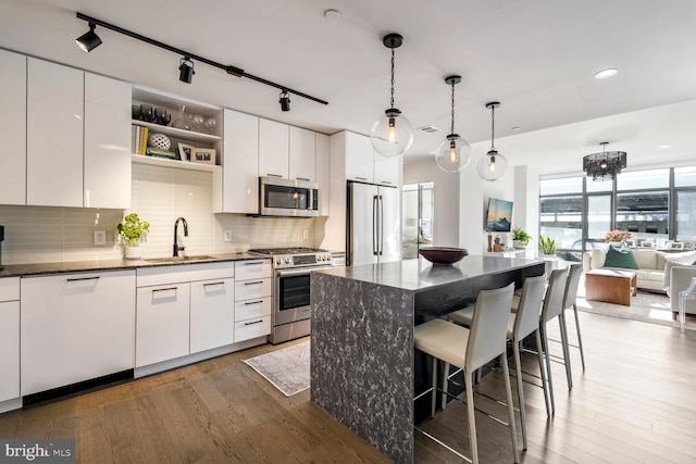 kitchen featuring a breakfast bar, wood finished floors, a sink, appliances with stainless steel finishes, and backsplash