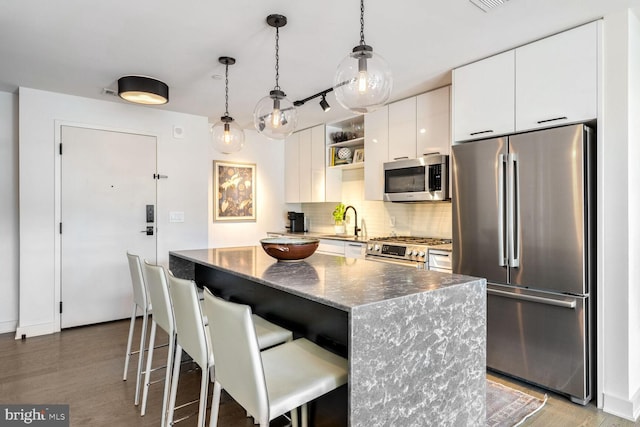 kitchen with stainless steel appliances, a breakfast bar, a sink, white cabinets, and tasteful backsplash