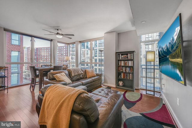 living room featuring ceiling fan, baseboards, a wall of windows, and wood finished floors