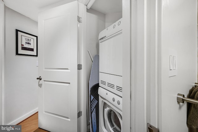 laundry room with laundry area, baseboards, wood finished floors, and stacked washer and clothes dryer