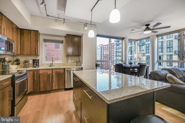 kitchen featuring stainless steel appliances, a sink, open floor plan, backsplash, and light wood finished floors