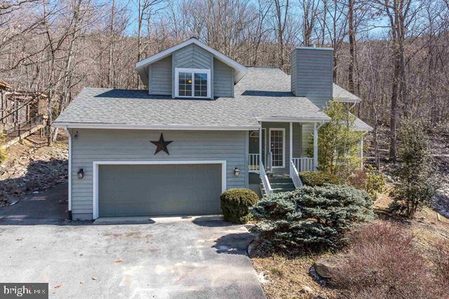 view of front facade featuring a porch, roof with shingles, driveway, and a chimney