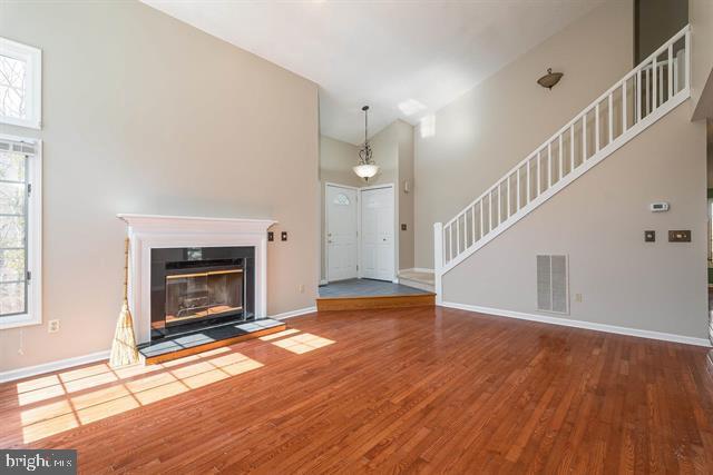 unfurnished living room with visible vents, stairway, a towering ceiling, wood finished floors, and baseboards