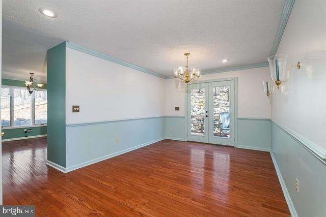 unfurnished dining area featuring wood finished floors, baseboards, french doors, an inviting chandelier, and crown molding