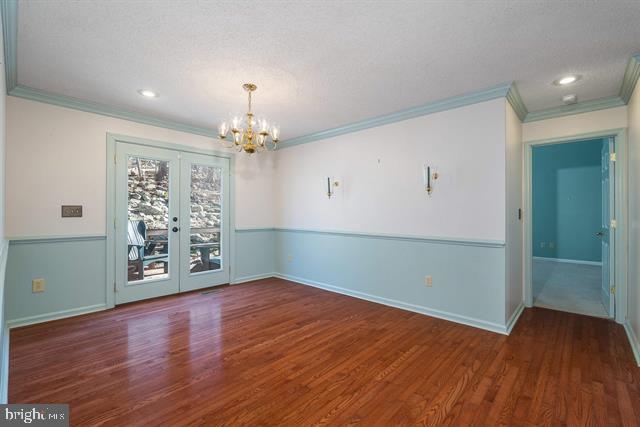 unfurnished dining area with a chandelier, french doors, crown molding, and wood finished floors