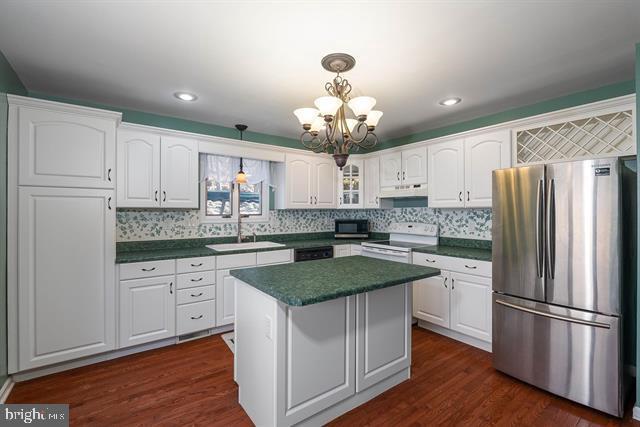 kitchen with white electric stove, white cabinets, dark countertops, freestanding refrigerator, and a sink