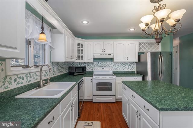 kitchen featuring white electric range oven, dark countertops, freestanding refrigerator, a sink, and under cabinet range hood