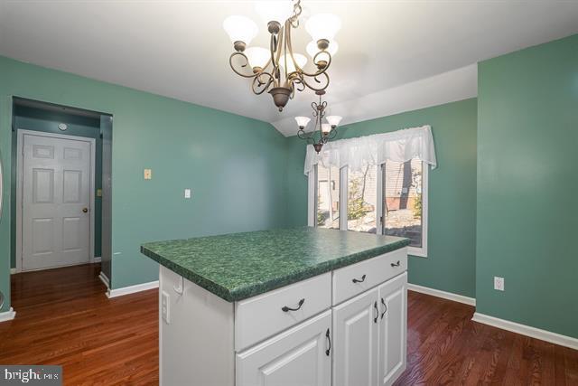 kitchen featuring dark wood-type flooring, dark countertops, baseboards, and an inviting chandelier