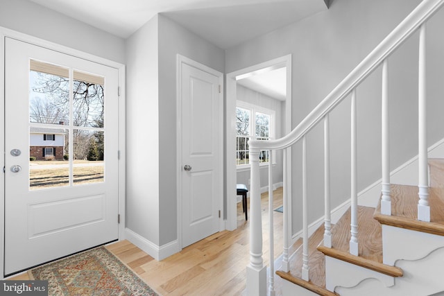 entryway with light wood-type flooring, stairway, and baseboards