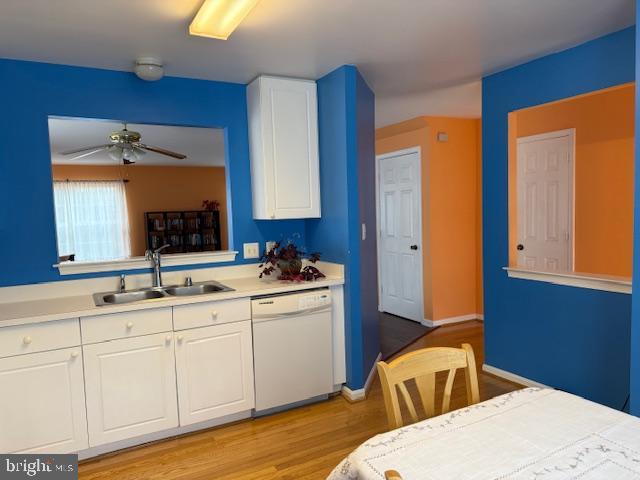 kitchen featuring white dishwasher, white cabinetry, light countertops, and a sink