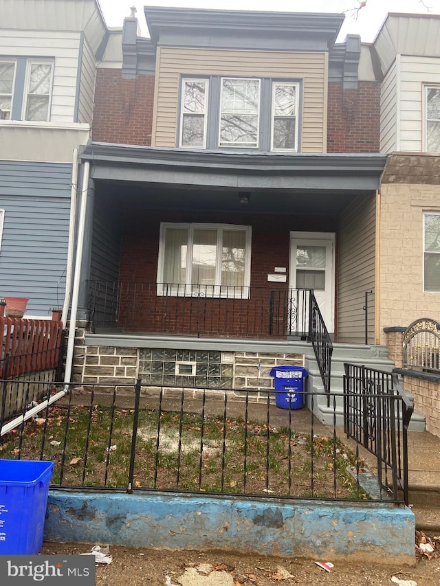 view of front of house featuring covered porch, brick siding, and a fenced front yard