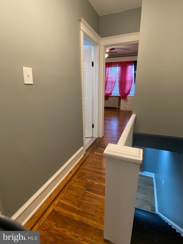 hallway with dark wood-style floors, radiator heating unit, an upstairs landing, and baseboards