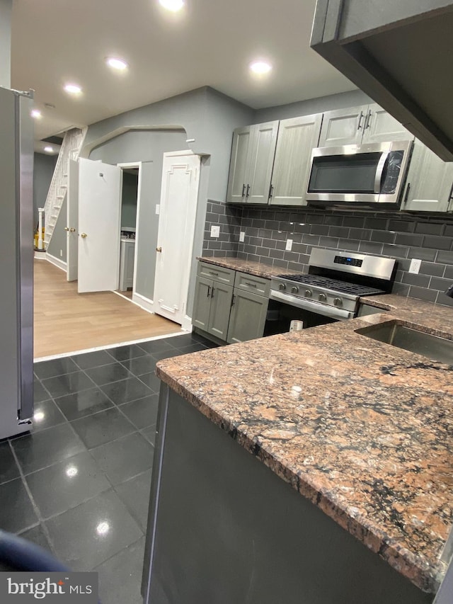 kitchen featuring stainless steel appliances, dark tile patterned flooring, a sink, and backsplash