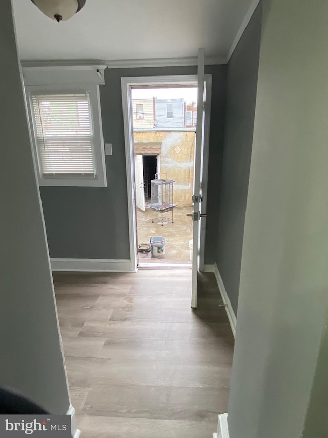 hall featuring crown molding, light wood-style floors, and baseboards