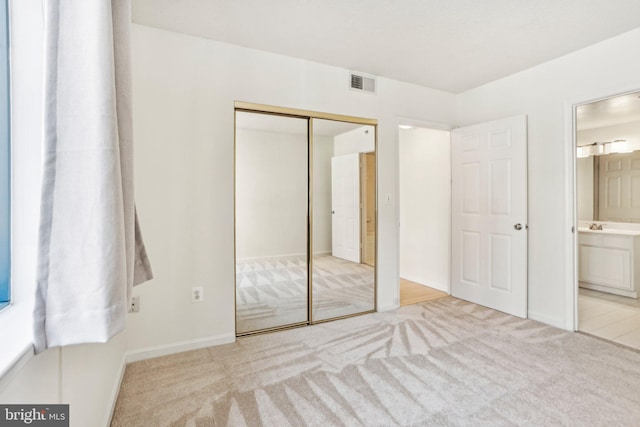 unfurnished bedroom featuring carpet floors, a closet, visible vents, ensuite bath, and baseboards