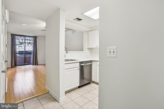 kitchen featuring light countertops, stainless steel dishwasher, white cabinetry, a sink, and light tile patterned flooring