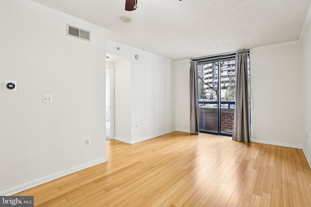 unfurnished room with ceiling fan, wood finished floors, visible vents, baseboards, and crown molding