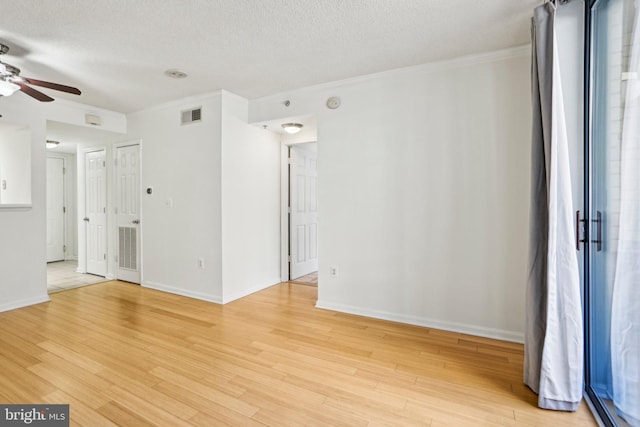 spare room featuring a textured ceiling, light wood-style flooring, visible vents, baseboards, and crown molding