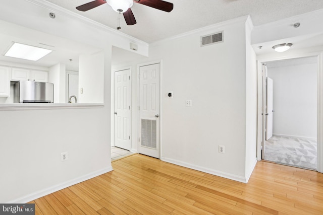 spare room with light wood-style floors, visible vents, crown molding, and baseboards