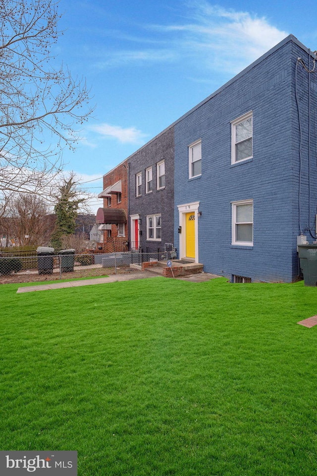 back of property with brick siding, a lawn, and fence