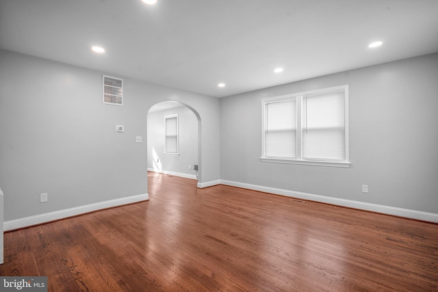 spare room featuring baseboards, arched walkways, wood finished floors, and recessed lighting