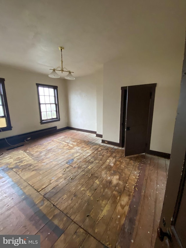 spare room featuring wood-type flooring, a notable chandelier, and baseboards