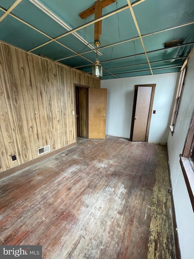 unfurnished room featuring wooden walls, visible vents, and hardwood / wood-style floors