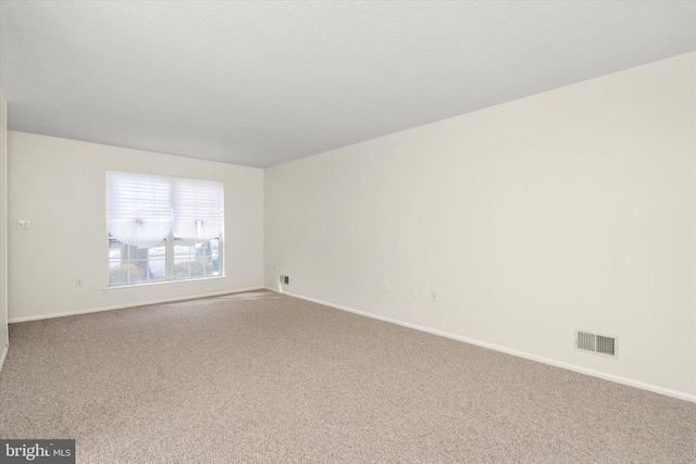 spare room with a textured ceiling, carpet, visible vents, and baseboards