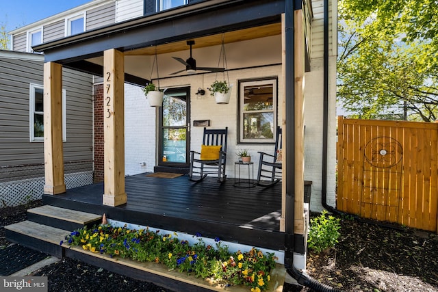 property entrance featuring a porch, brick siding, fence, and a ceiling fan