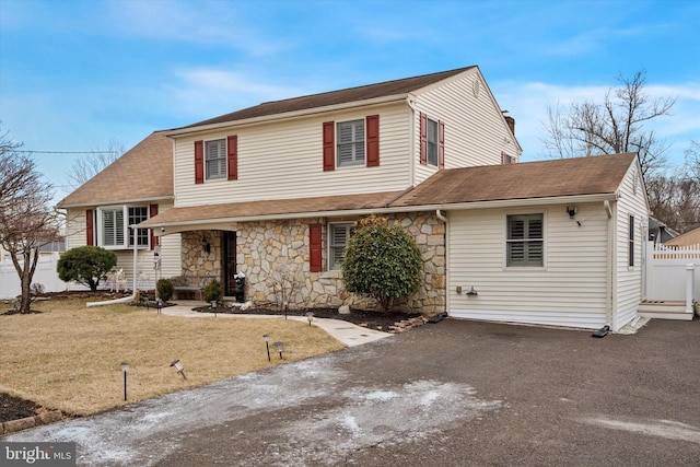 tri-level home featuring stone siding, driveway, a front lawn, and fence