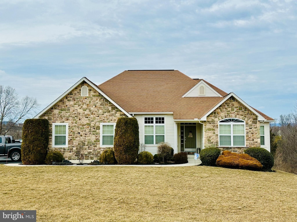 view of front of house with stone siding, a front lawn, and roof with shingles