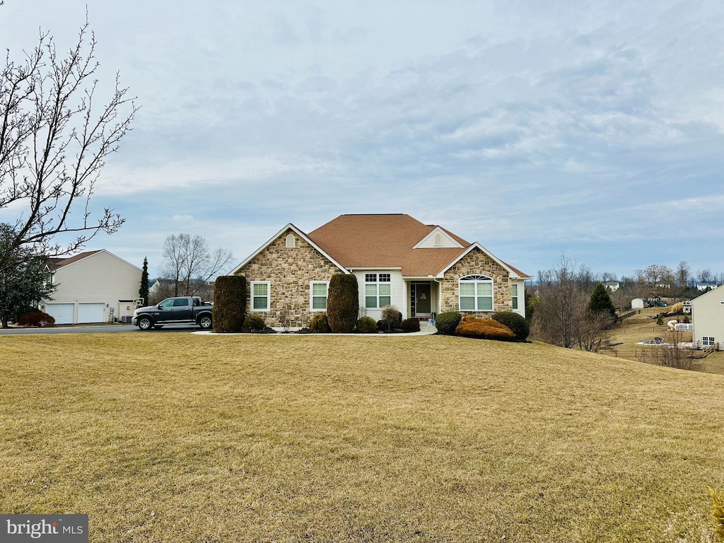 view of front of property with stone siding, a detached garage, and a front yard