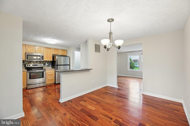 kitchen featuring appliances with stainless steel finishes, a textured ceiling, dark wood-style flooring, a chandelier, and backsplash