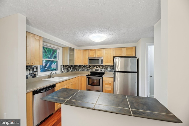 kitchen featuring appliances with stainless steel finishes, a sink, light brown cabinets, a textured ceiling, and backsplash